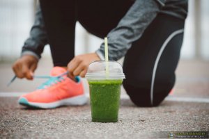 Detox Smoothie Drink And Running Footwear Close Up. City Outdoor Workout And Fitness Healthy Nutrition Concept. Female Athlete Tying Sport Shoes Laces Before Training.